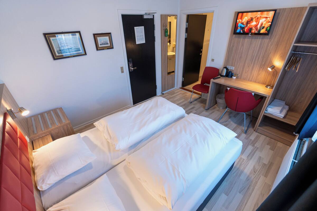 A hotel room with two beds, a desk, a chair, a TV, and a bathroom visible through an open door.