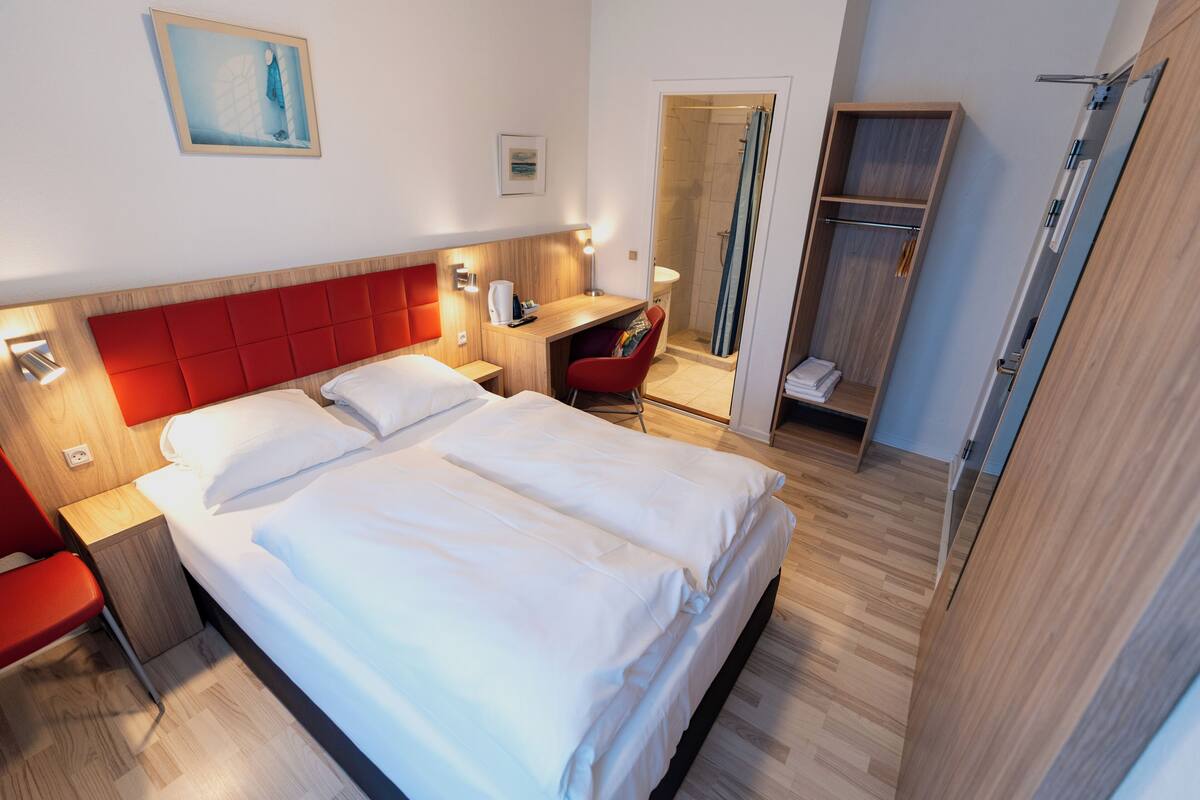 A hotel room with a large bed, a desk, a chair, a shower area, and a wardrobe.