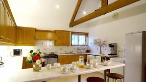 A kitchen with wooden cabinets, a central island with stools, and a refrigerator. - The Coachman's Quarters at Muncaster Castle (Ravenglass)