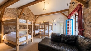 A rustic room with wooden bunk beds, a leather sofa, stone walls, and a chandelier. - The Coachman's Quarters at Muncaster Castle (Ravenglass)