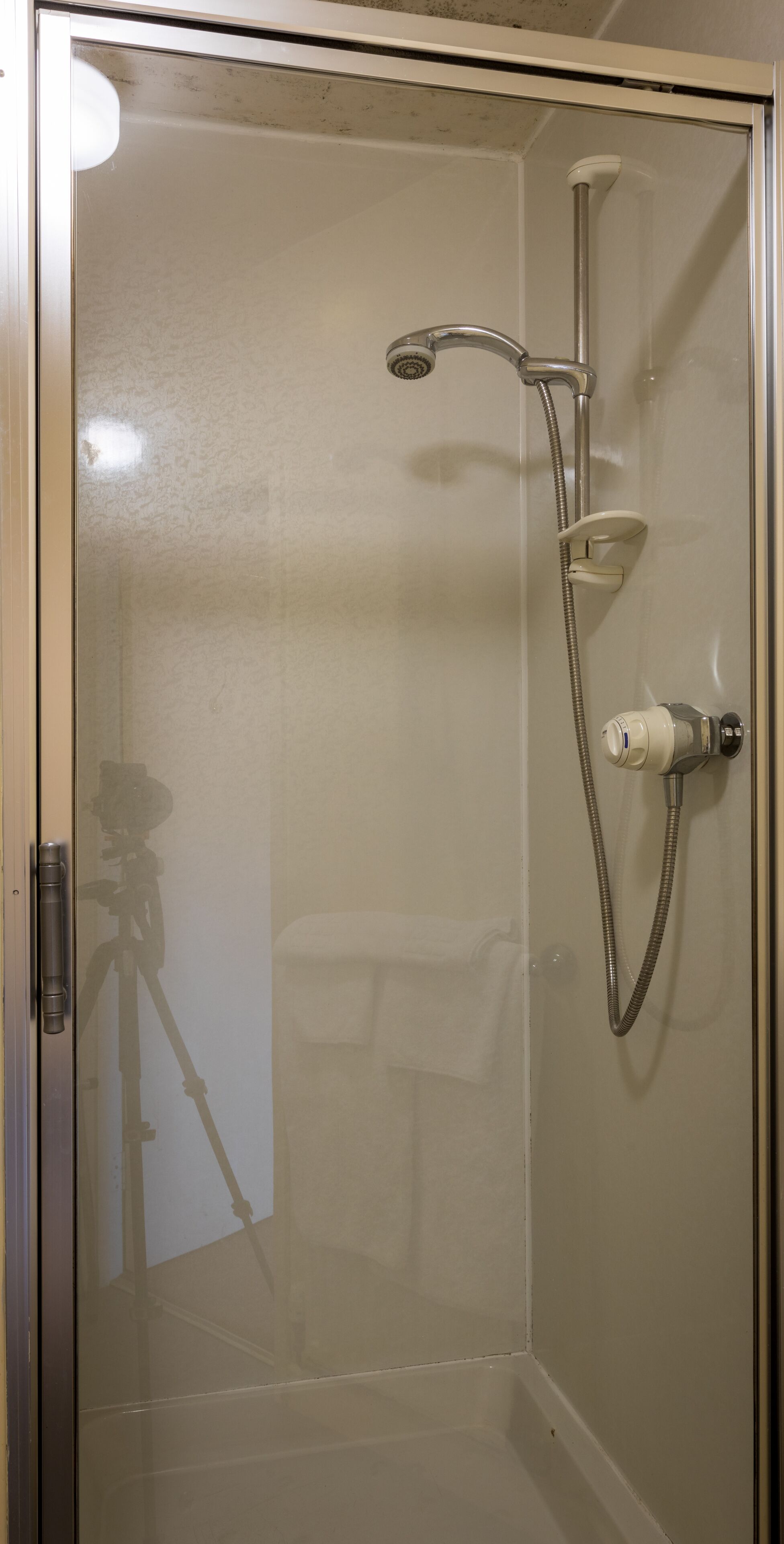 A glass-enclosed shower stall with a handheld showerhead and a wall-mounted faucet.
