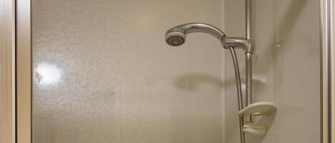 A glass-enclosed shower stall with a handheld showerhead and a wall-mounted faucet.