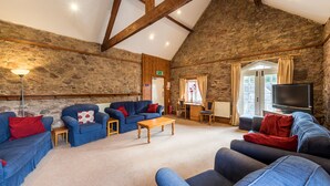 A cozy room with stone walls, wooden beams, and blue sofas with red cushions. - The Coachman's Quarters at Muncaster Castle (Ravenglass)