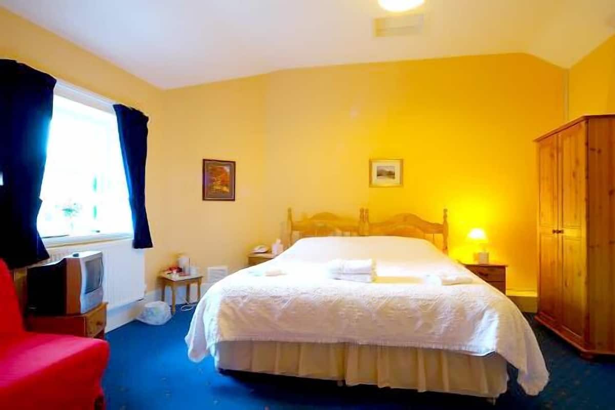 A hotel room with a large bed, a wooden wardrobe, a red chair, and a window with curtains.