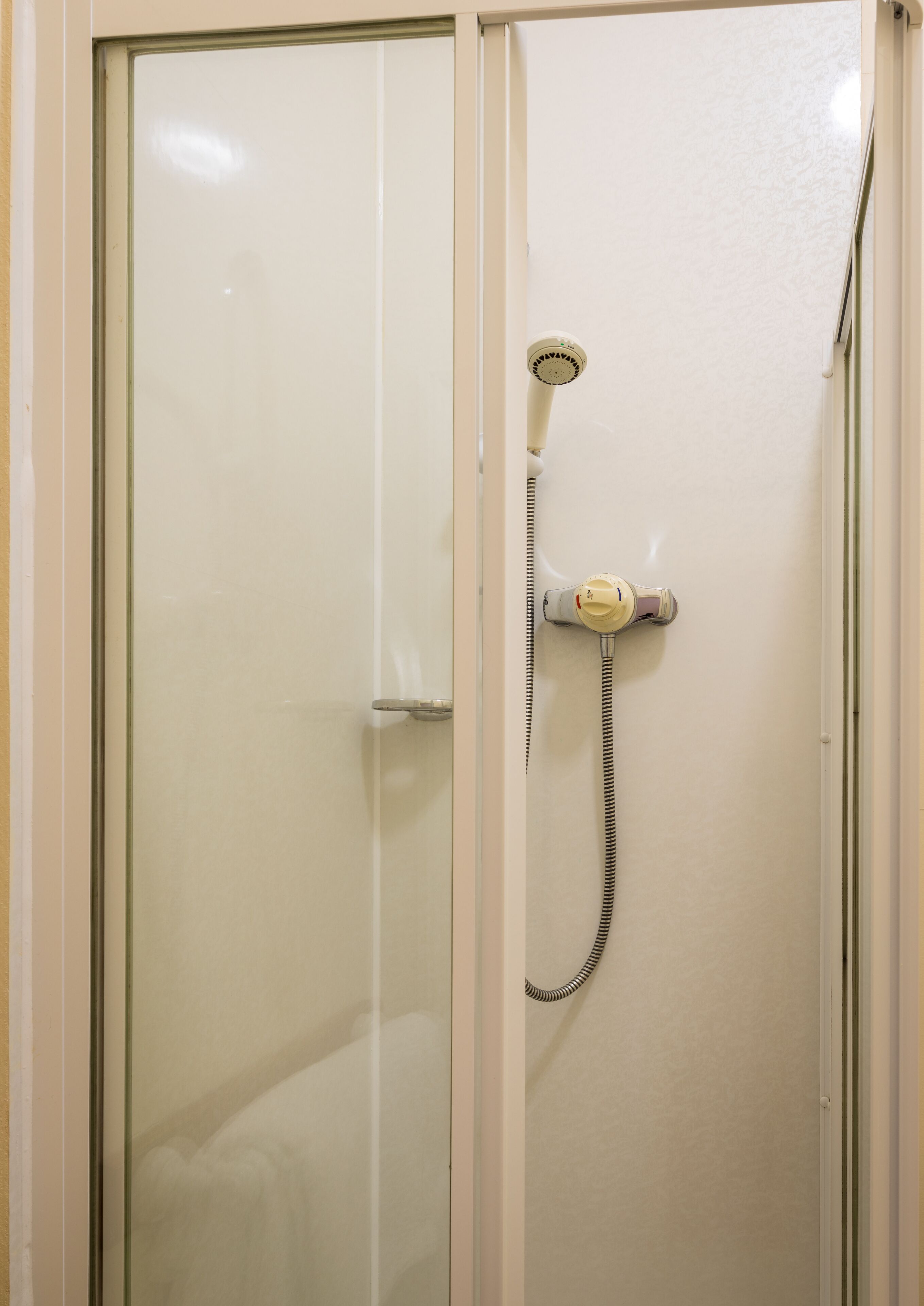 Une cabine de douche fermée par des parois en verre, dotée d’un pommeau de douche à main et d’un flexible.