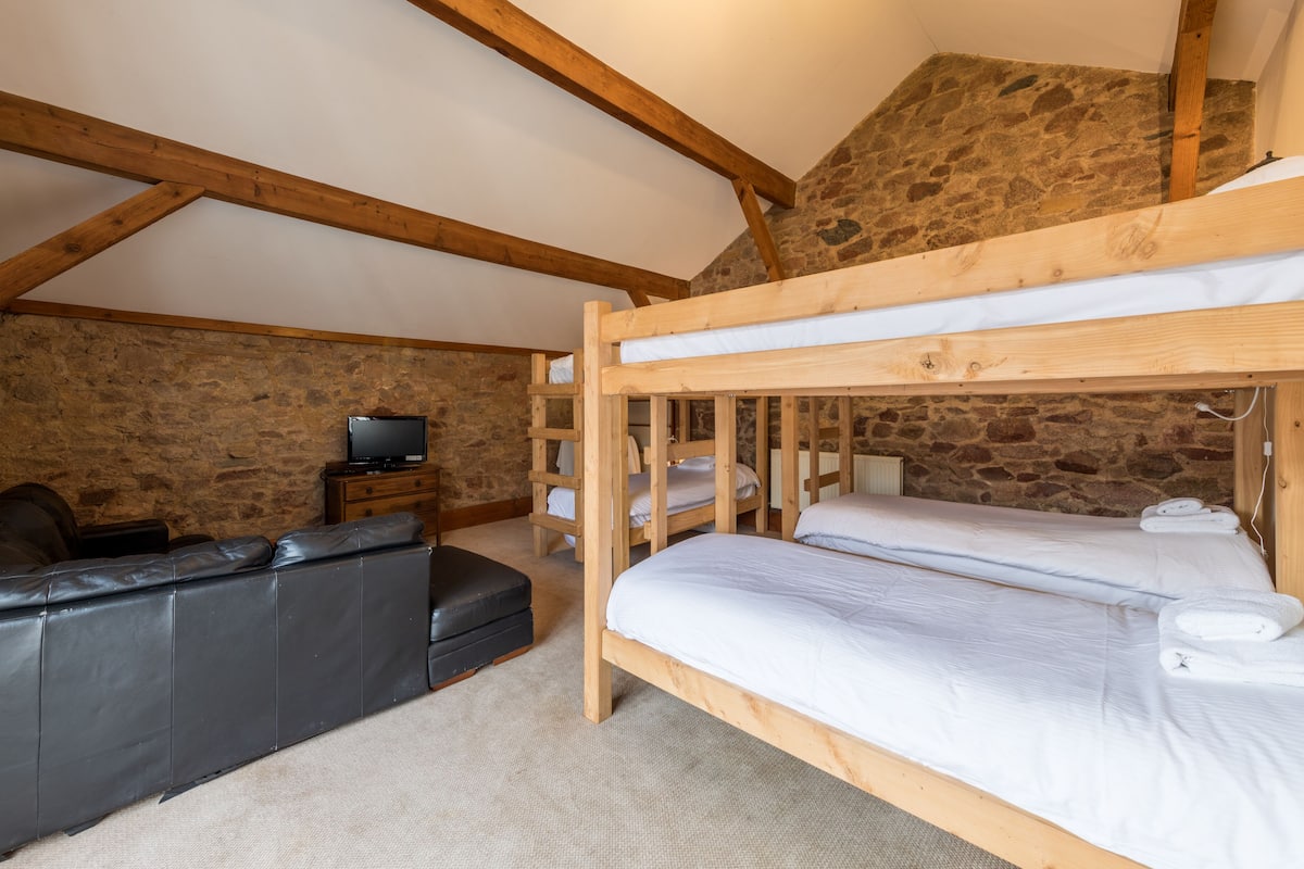 A rustic room with a bunk bed, a leather sofa, and a stone wall.
