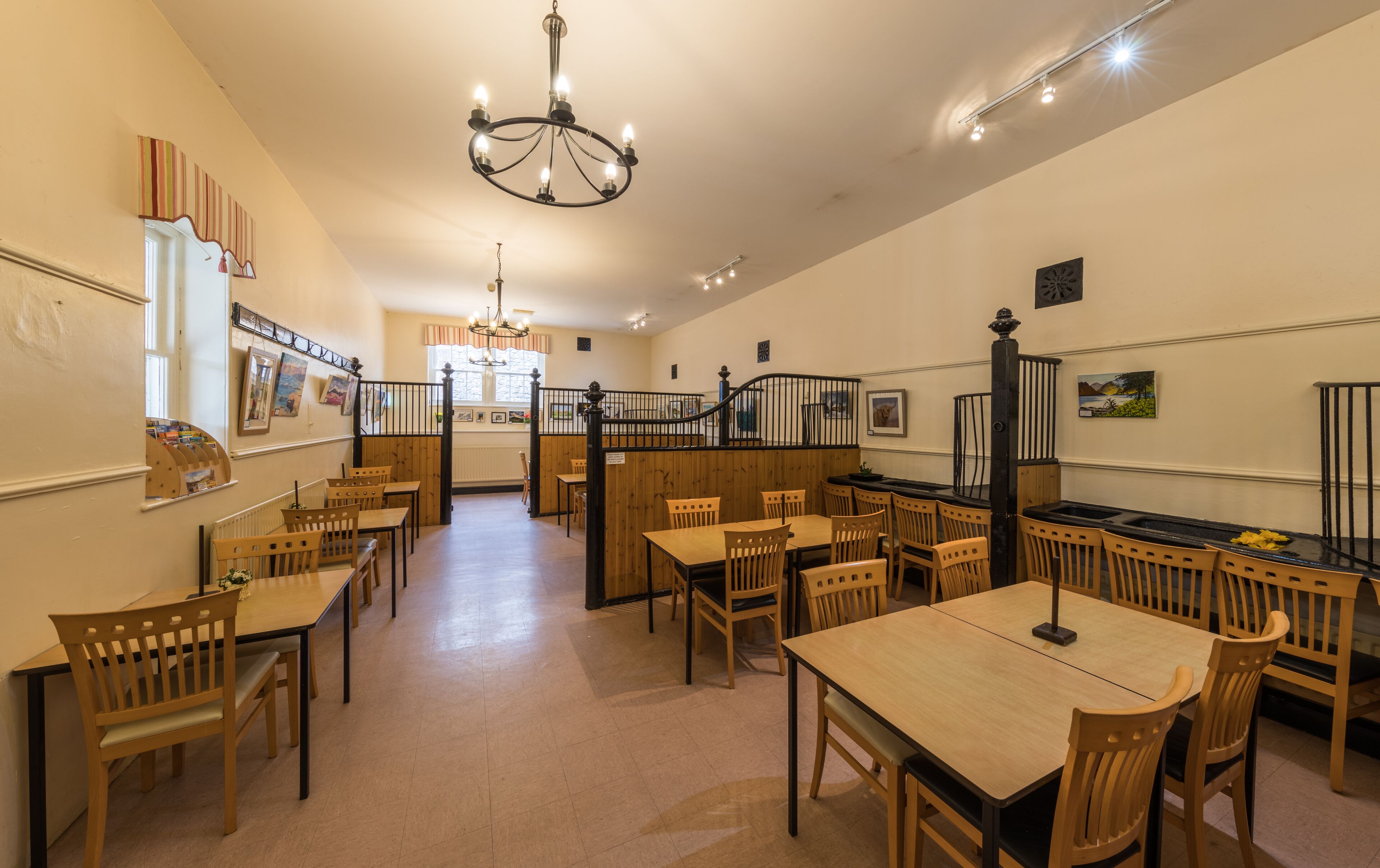 A dining area with wooden tables and chairs, a chandelier, and artwork on the walls.