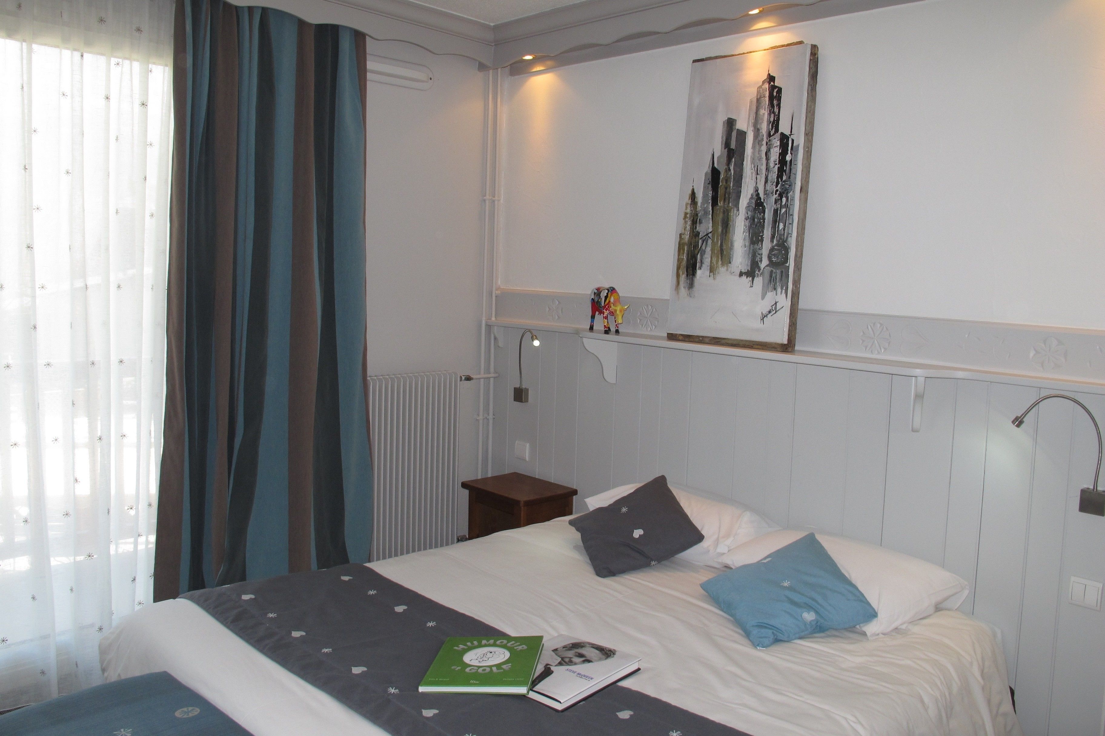 A neatly made bed with pillows and a book, a small nightstand, a radiator, and a wall-mounted artwork.