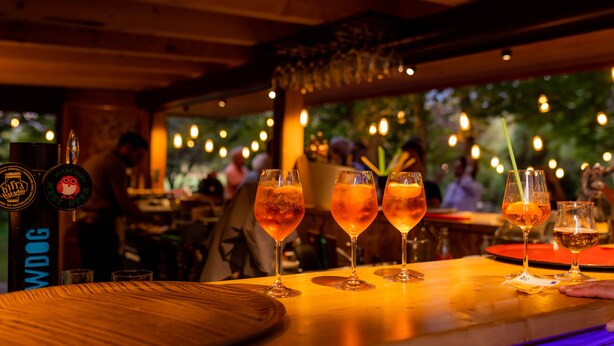Un rincón de bar con mesas de madera y vasos de bebidas ámbar.