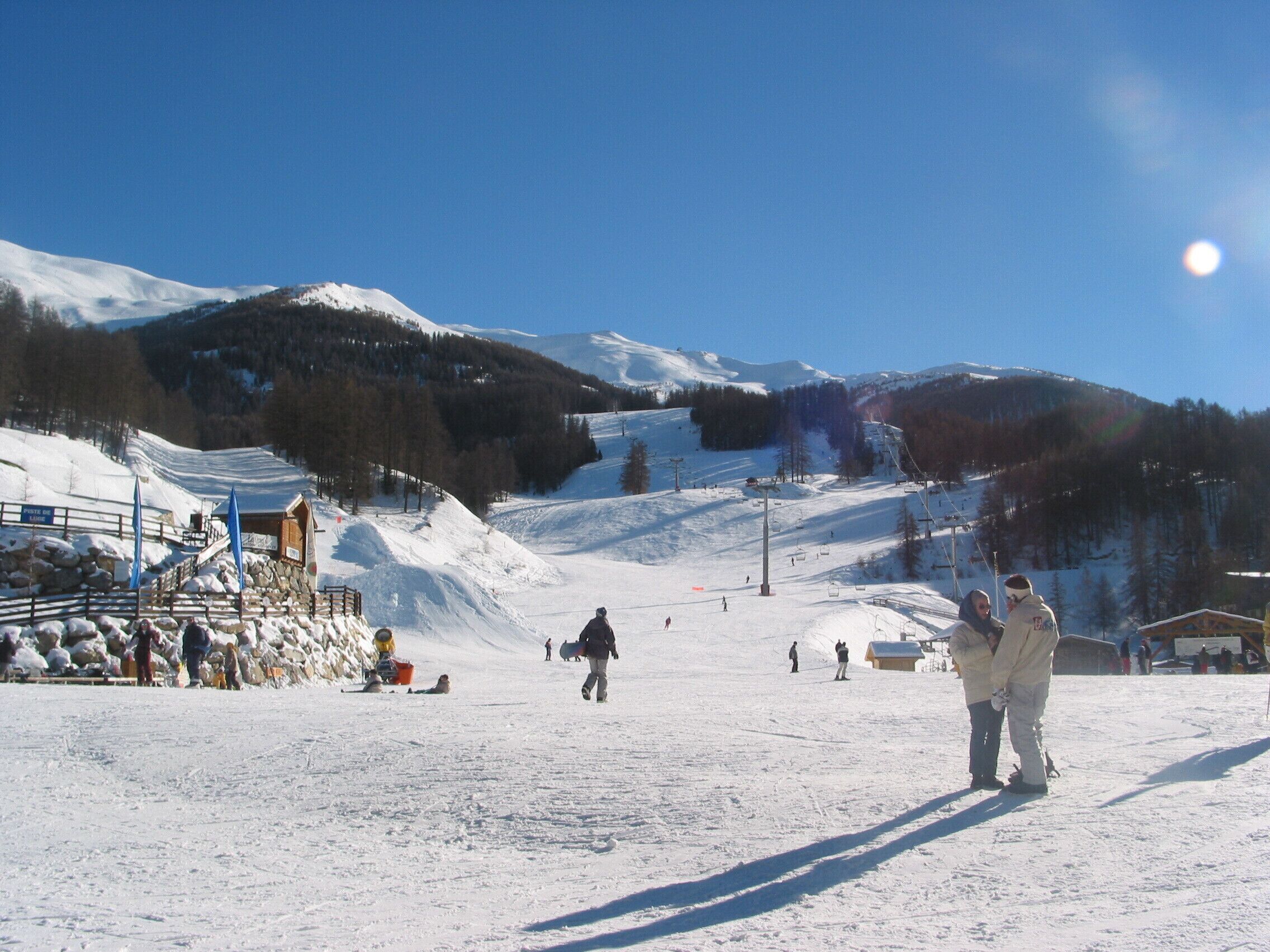 A ski resort with a snow-covered slope, a ski lift, and a clear blue sky.