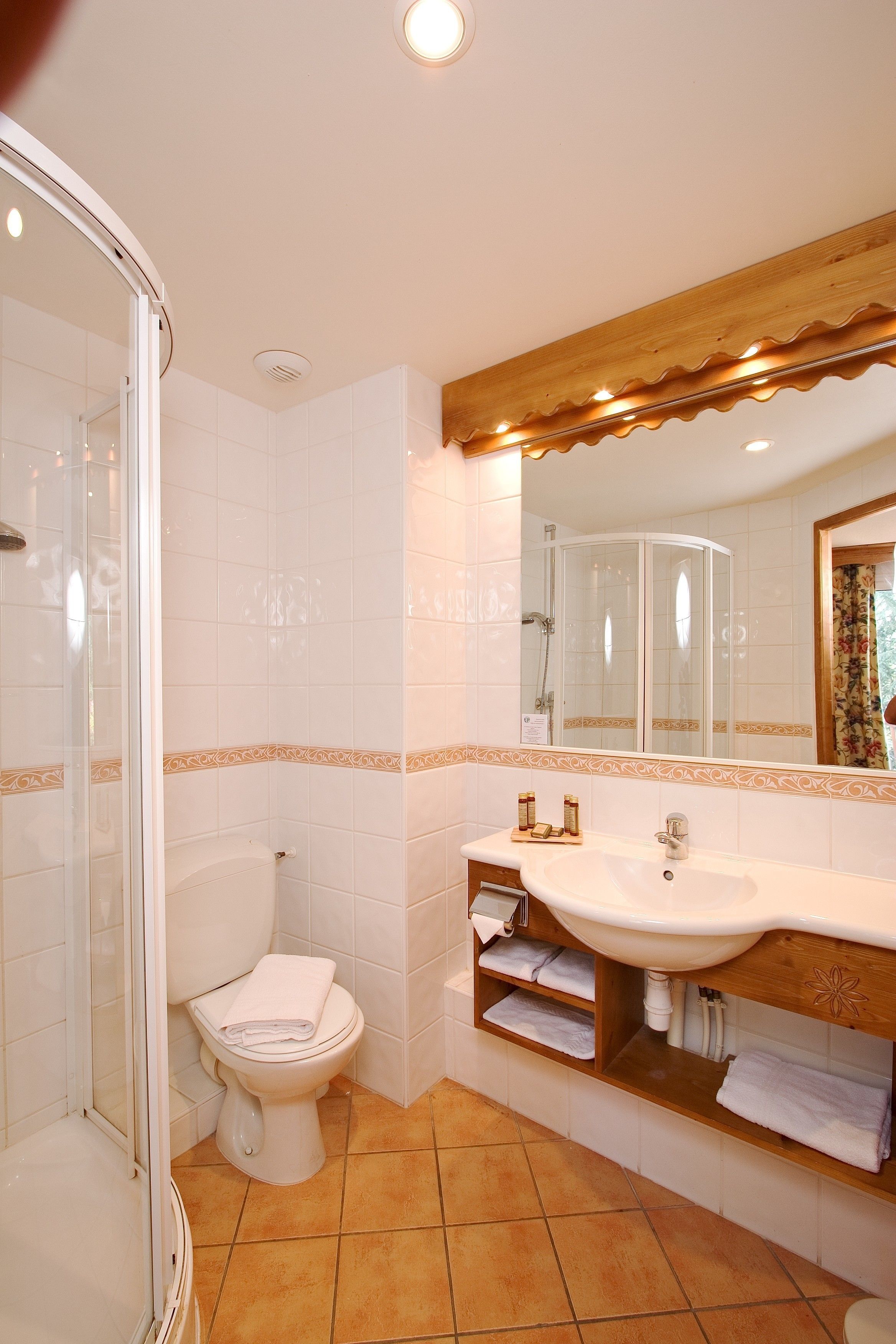 A bathroom with a glass shower enclosure, a white toilet, a sink with a wooden vanity, and a mirror with a decorative frame.