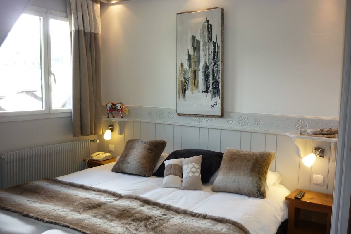 A hotel room with a bed, a painting, a nightstand, a lamp, and a window with curtains.