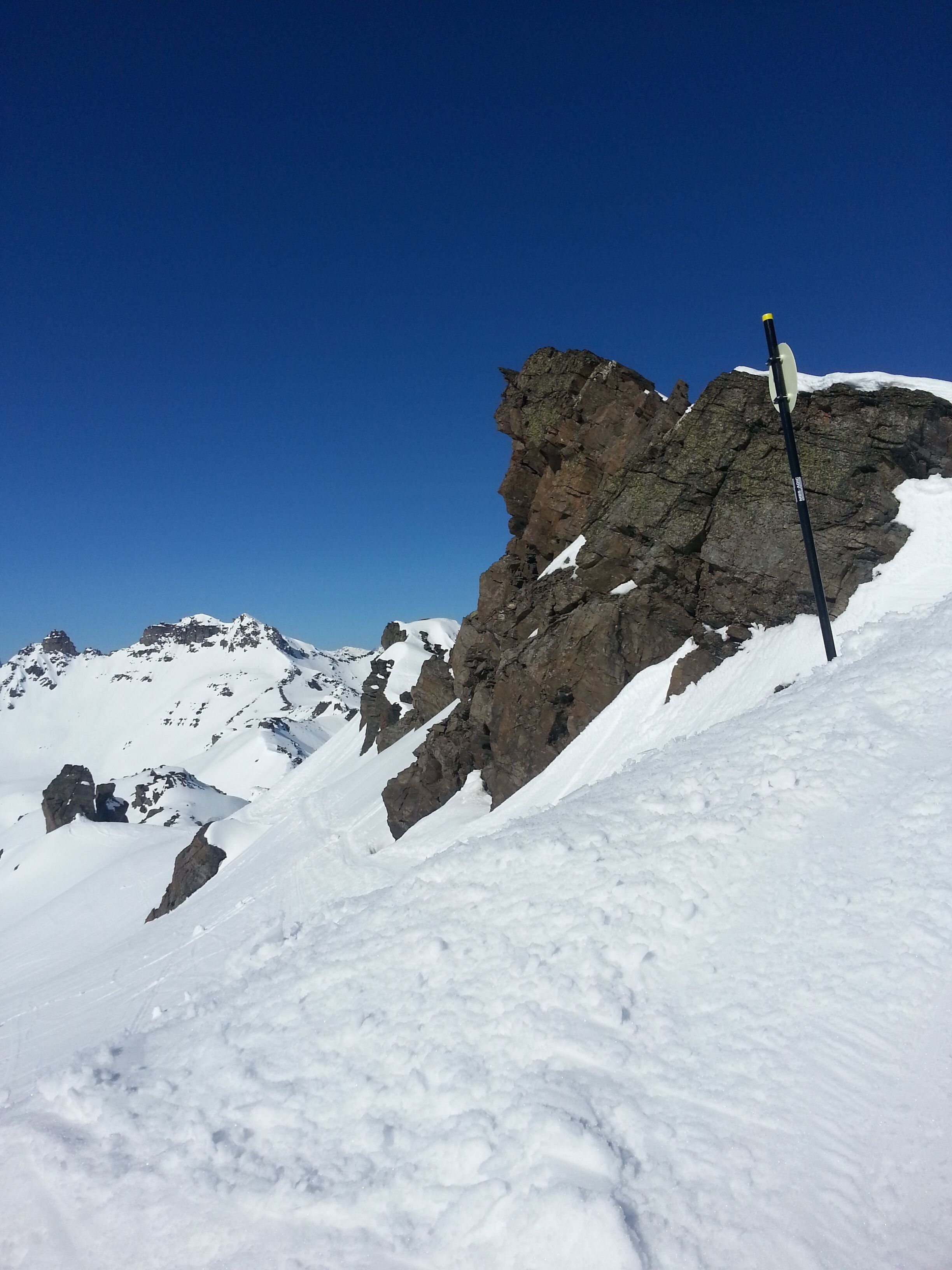 A snow-covered mountain with rocky outcrops and a clear blue sky.