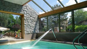 Una piscina interior con pared de piedra y ventanas amplias.