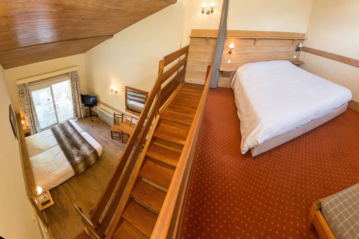 A bedroom with a large bed, wooden flooring, a small desk, and a window with curtains.