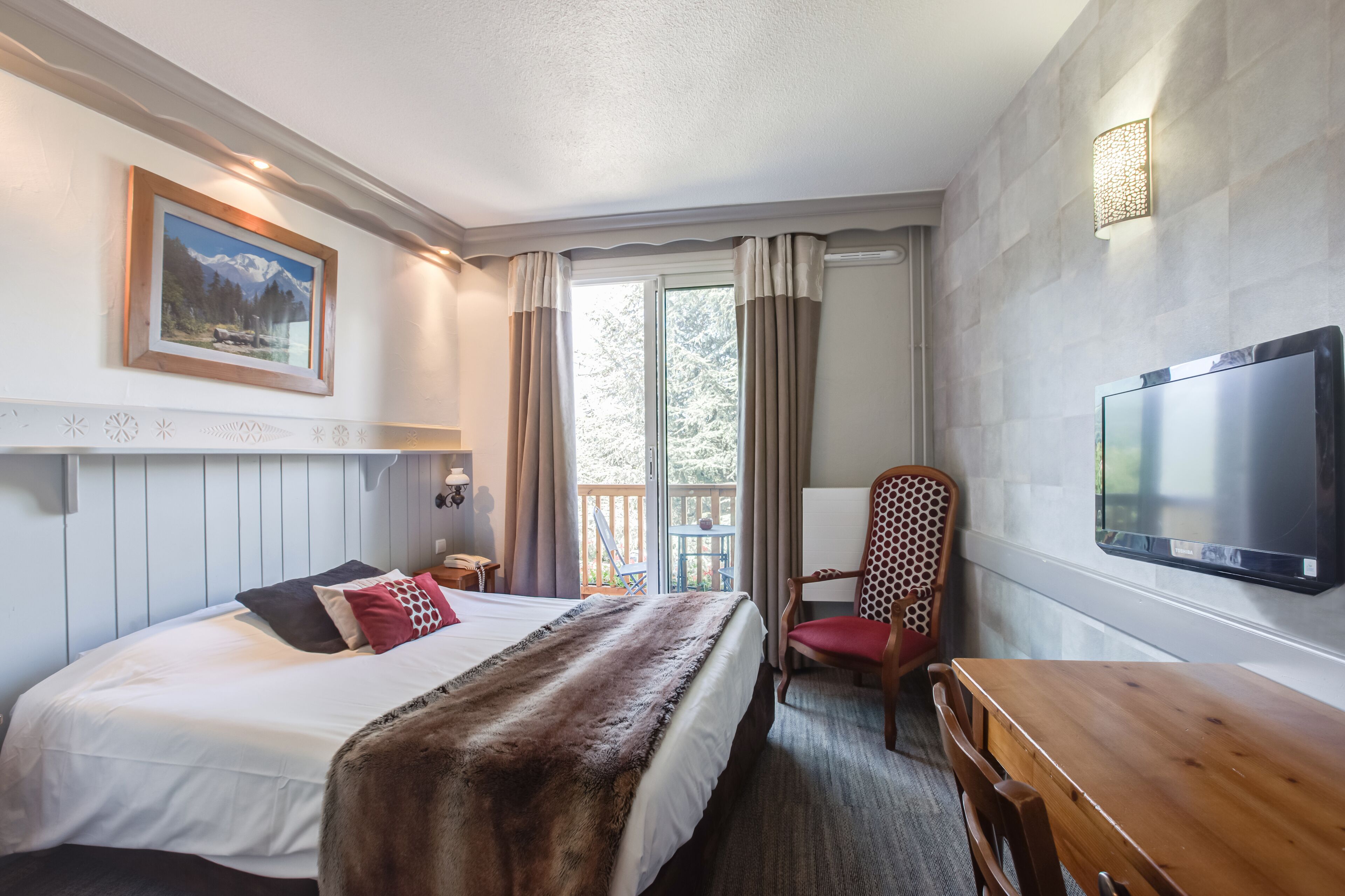 A hotel room with a bed, a wooden desk, a chair, a television, and a window with curtains.
