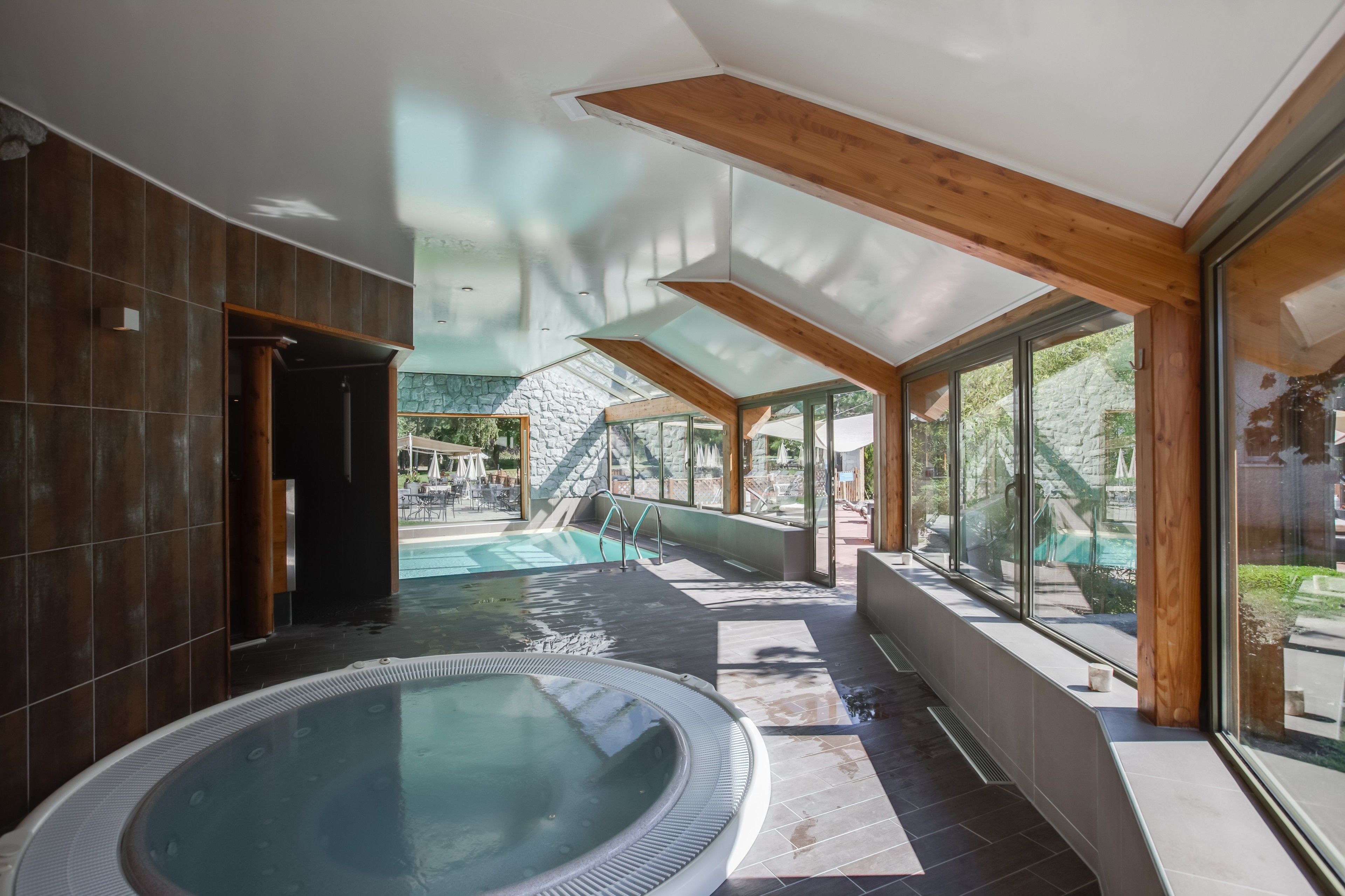 Un área de piscina interior moderna con un jacuzzi, ventanas amplias y una pared de piedra al fondo.