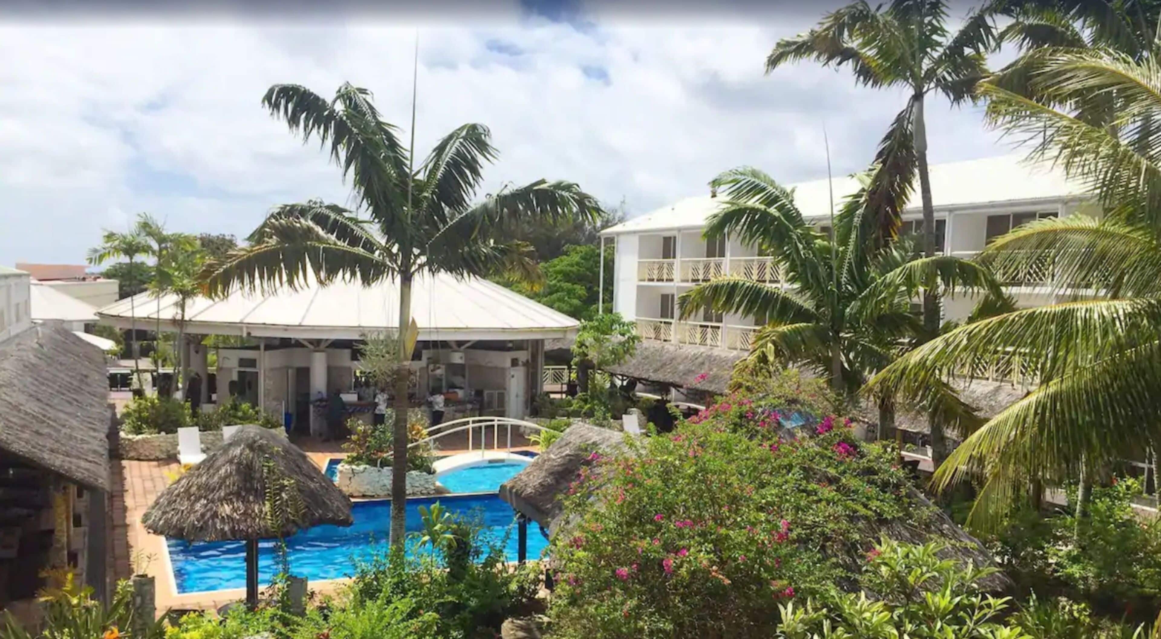 A resort with a swimming pool, thatched-roof structures, and lush greenery.