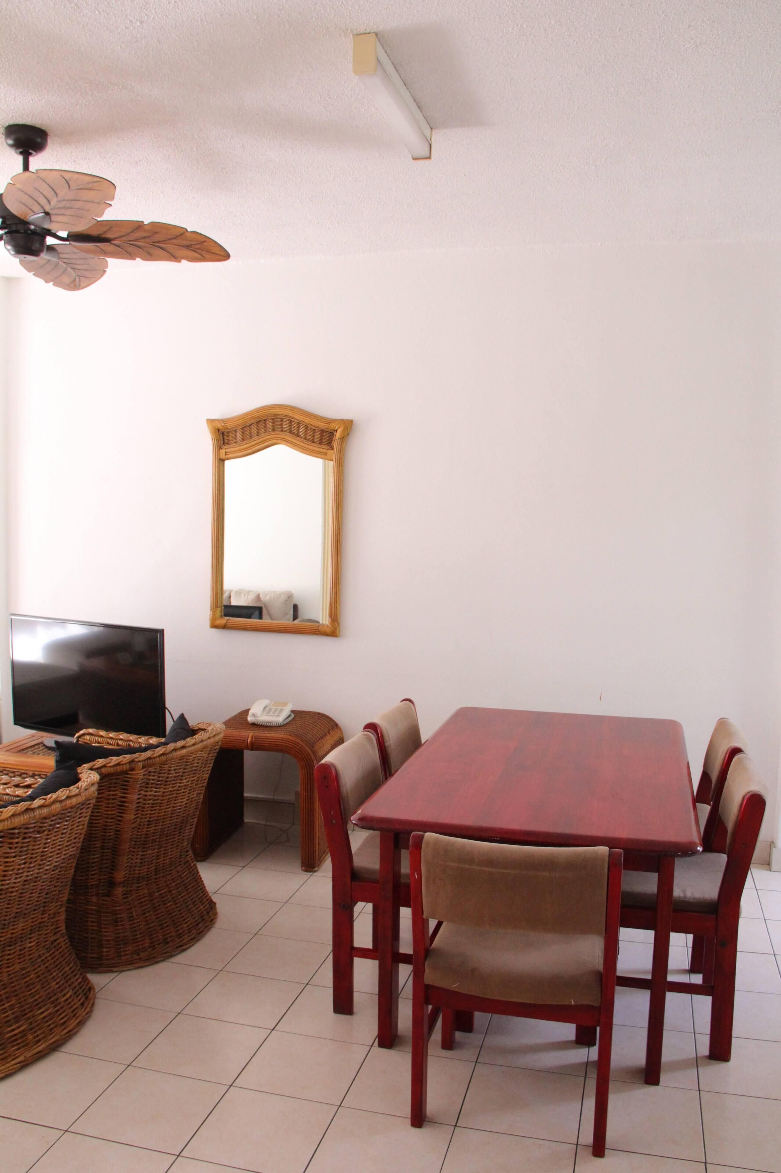 A dining area with a wooden table, six chairs, a television, a telephone, and wicker baskets.