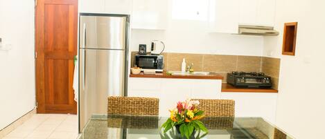 A modern kitchen with a stainless steel refrigerator, microwave, and toaster. There is a glass dining table with a vase of flowers.