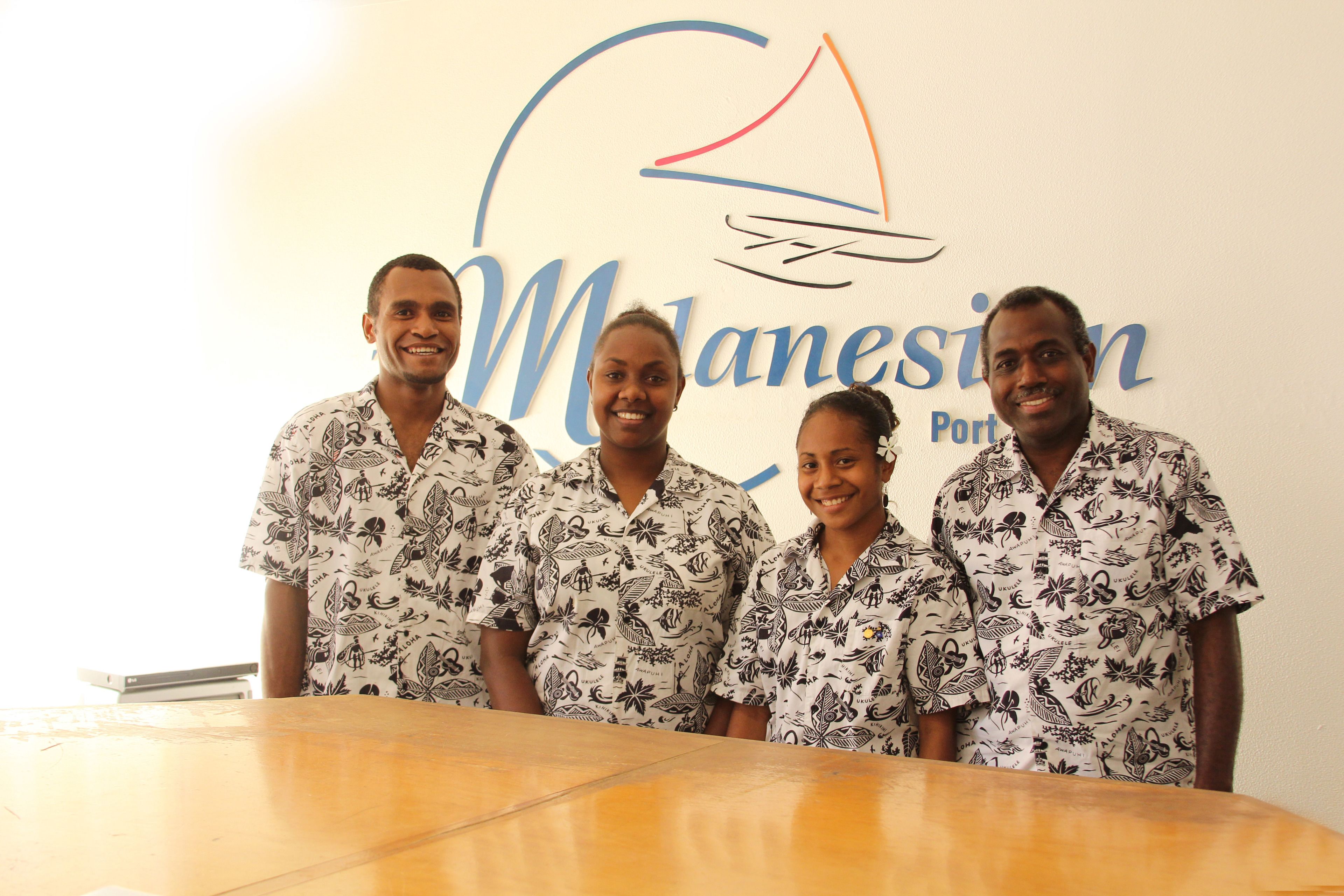 Four people standing in front of a wall with a logo and text that reads "Mlanesin Port".