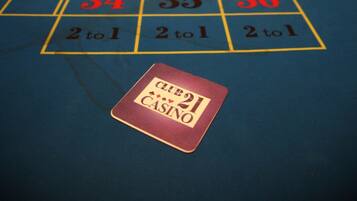 A craps table with numbers and "2 to 1" bets, a "Club Casino" placard, and a person in the background.