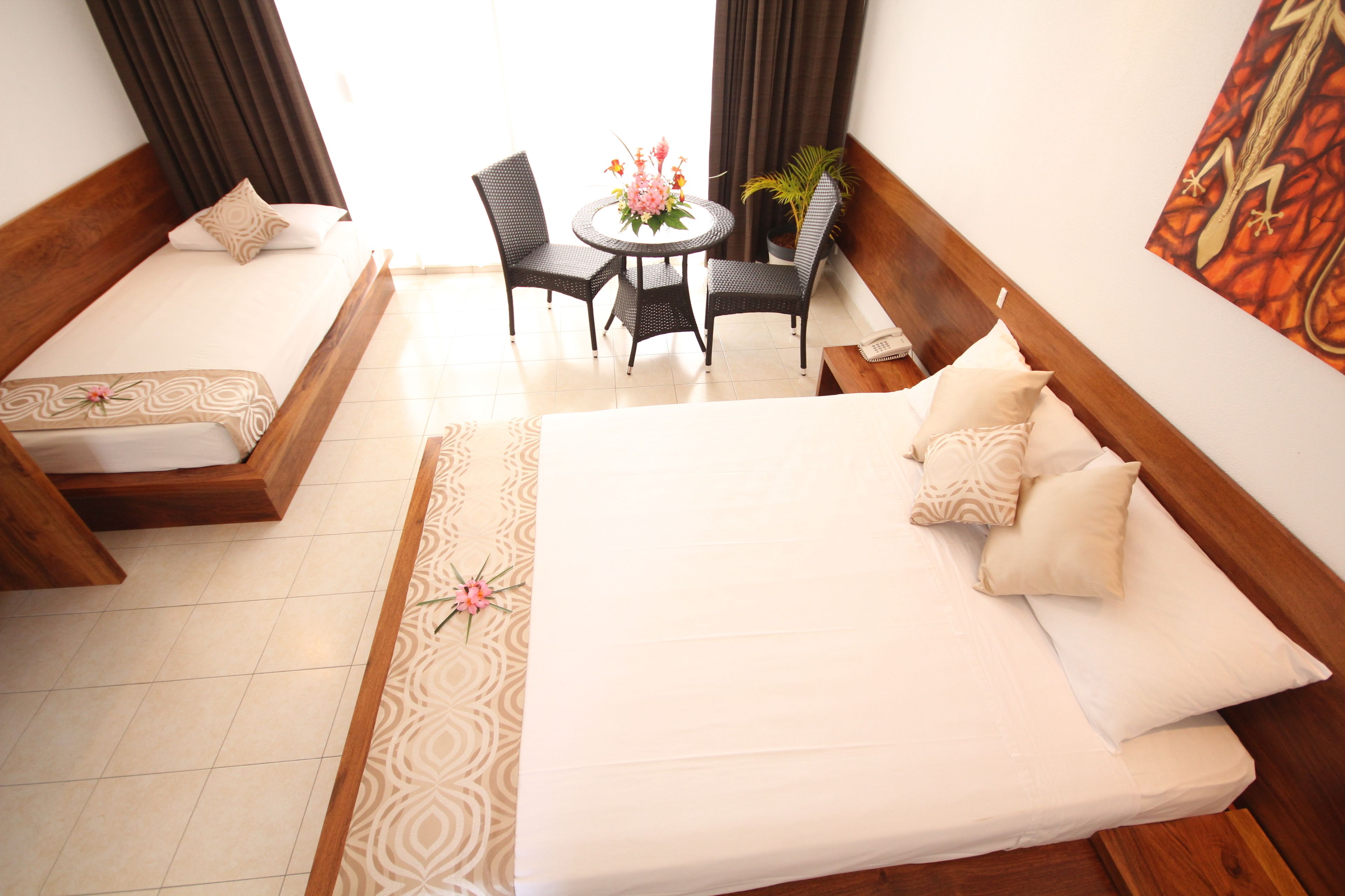 A hotel room with a large bed, two bedside tables, a round table with chairs, and a potted plant.