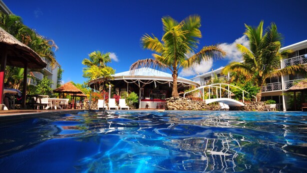 A swimming pool with a tropical setting, including palm trees and a covered area with seating. - The Melanesian Port Vila Hotel (Port Vila)