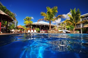 A swimming pool with a tropical setting, including palm trees and a covered area with seating. - The Melanesian Port Vila Hotel (Port Vila)