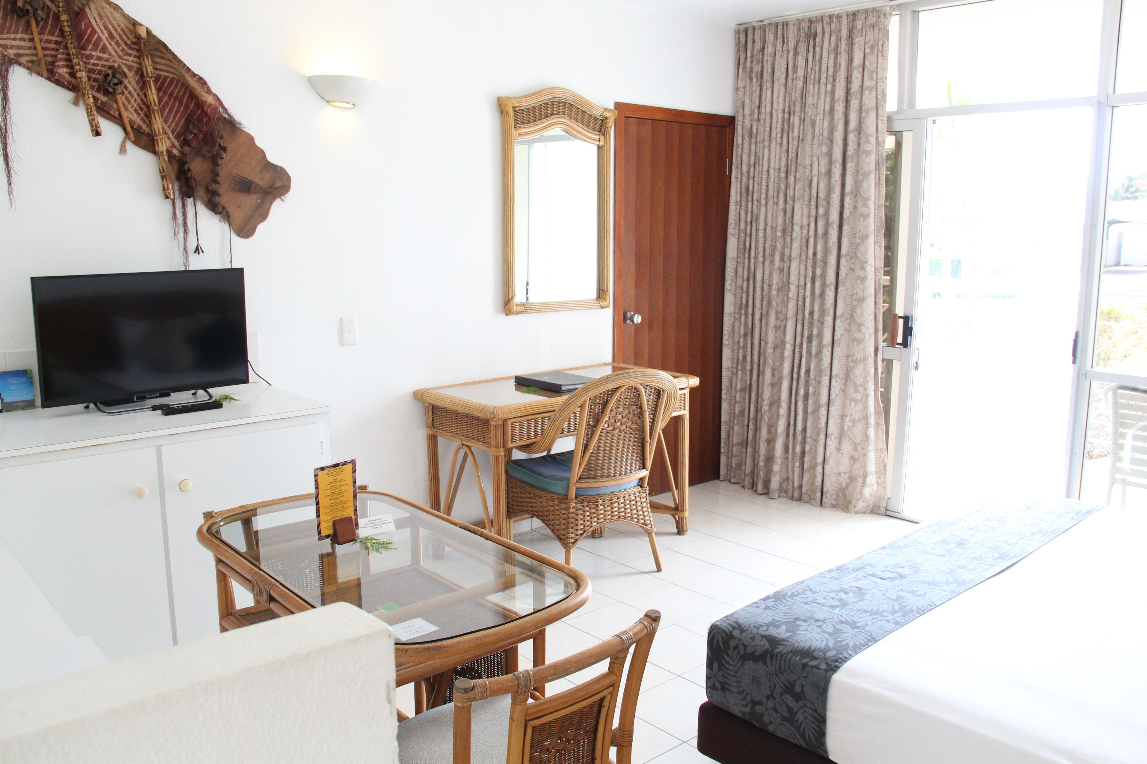 A hotel room with a bed, a desk with a chair, a television, and a large mirror.