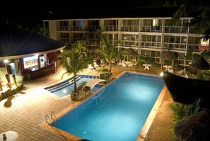 A swimming pool area with a bar, lounge chairs, and a building with balconies in the background. - The Melanesian Port Vila Hotel (Port Vila)