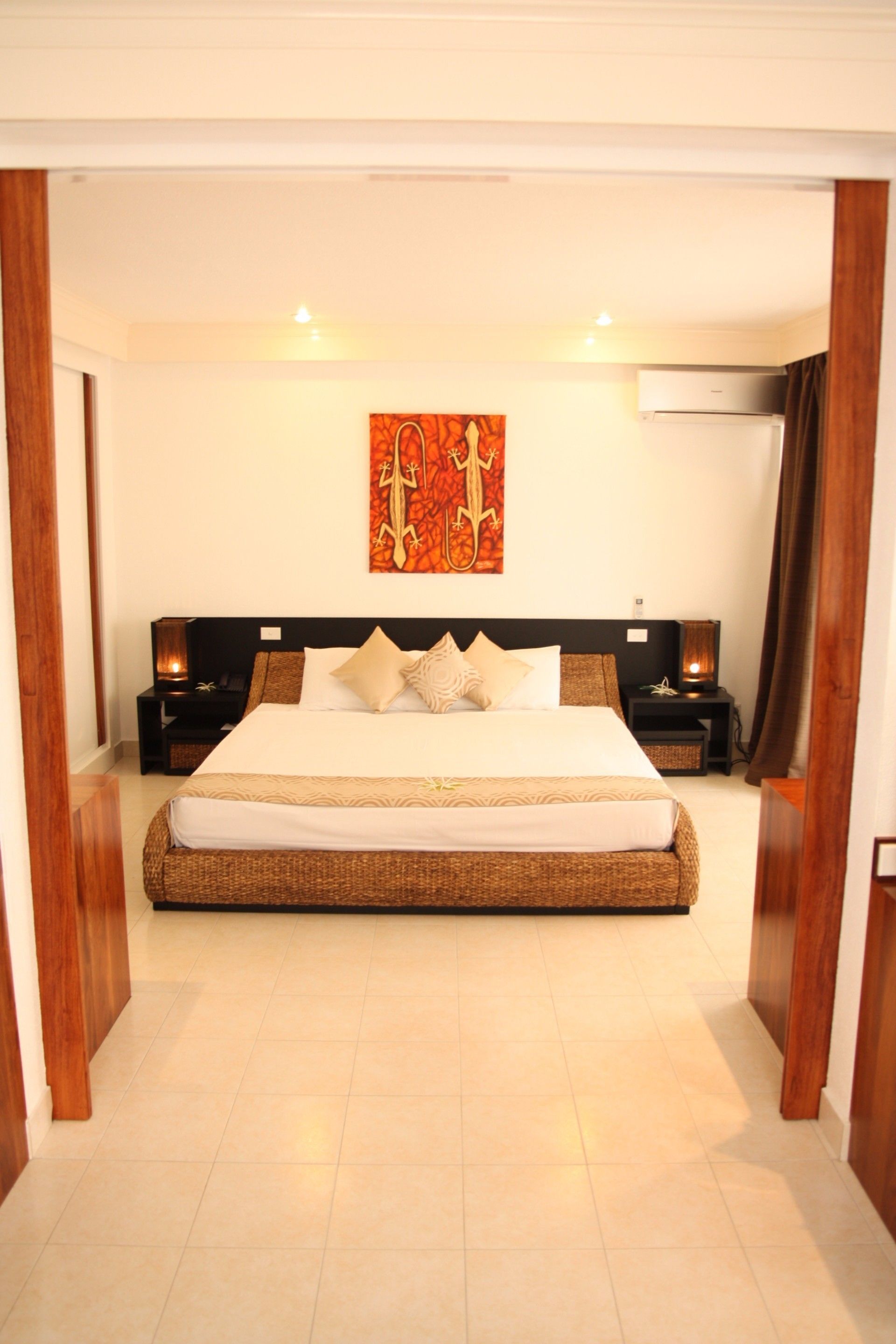 A spacious bedroom with a large bed, two bedside tables with lamps, a wall-mounted artwork, and a ceiling fan.