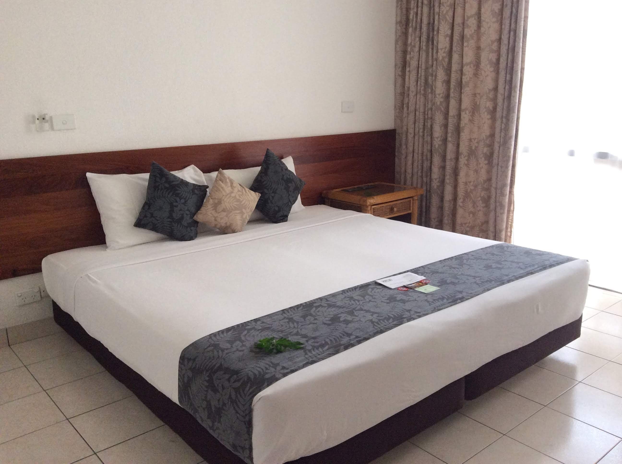 A neatly made bed with a white duvet and a grey floral bedspread, accompanied by several pillows in different patterns.