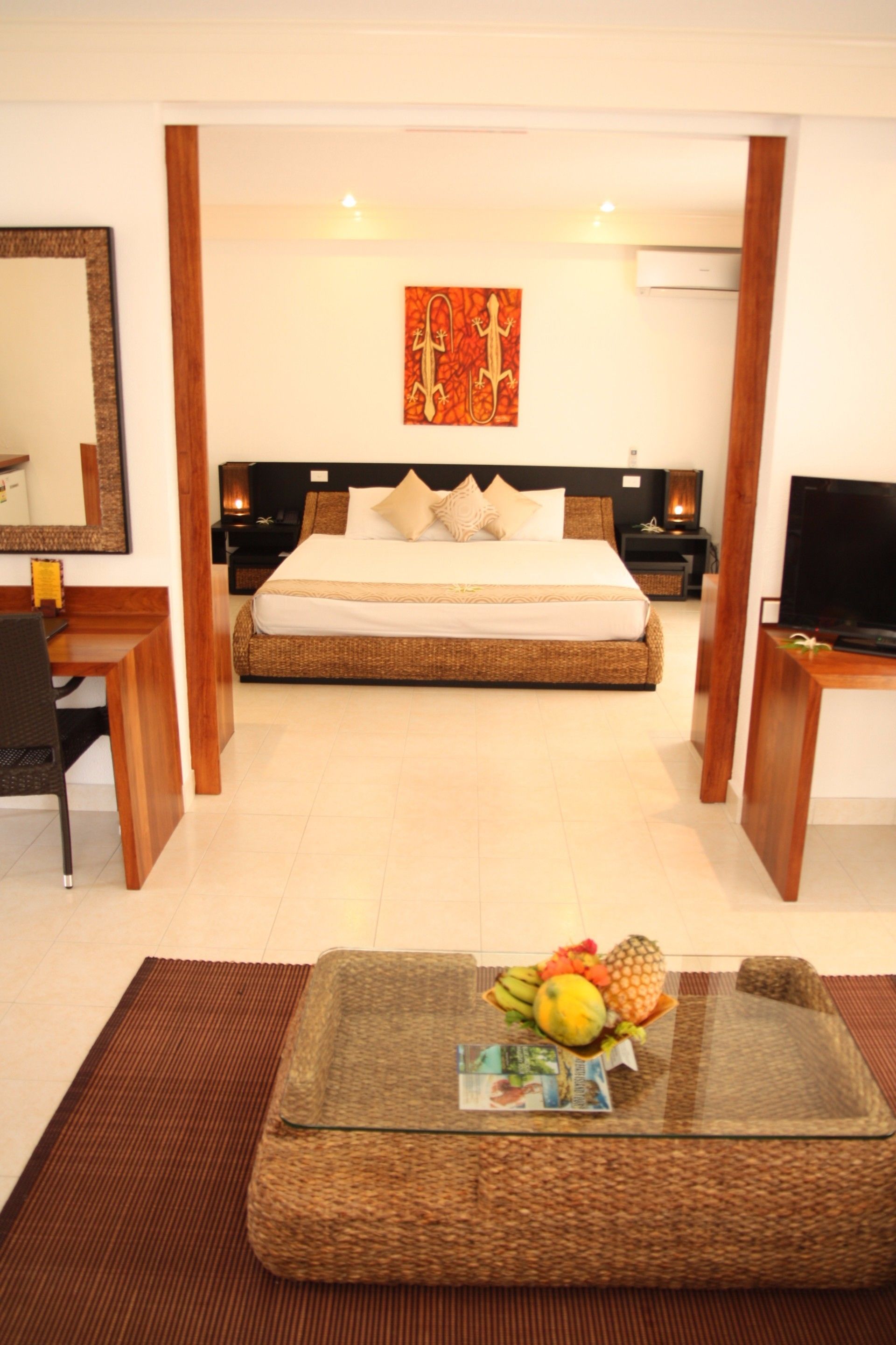 A hotel room with a bed, bedside tables, a TV, a desk, and a coffee table with fruit.