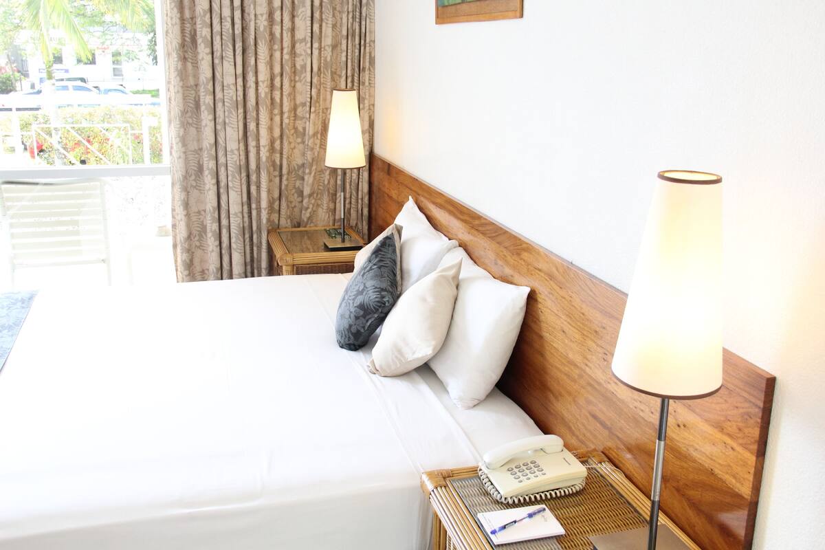 A hotel room with a bed, a bedside lamp, a telephone, and a notepad on the nightstand.