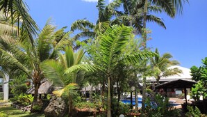 A tropical garden with palm trees, a swimming pool, and a thatched-roof structure. - The Melanesian Port Vila Hotel (Port Vila)