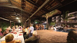An outdoor dining area with tables and chairs, a pool, and a building with balconies in the background. - The Melanesian Port Vila Hotel (Port Vila)