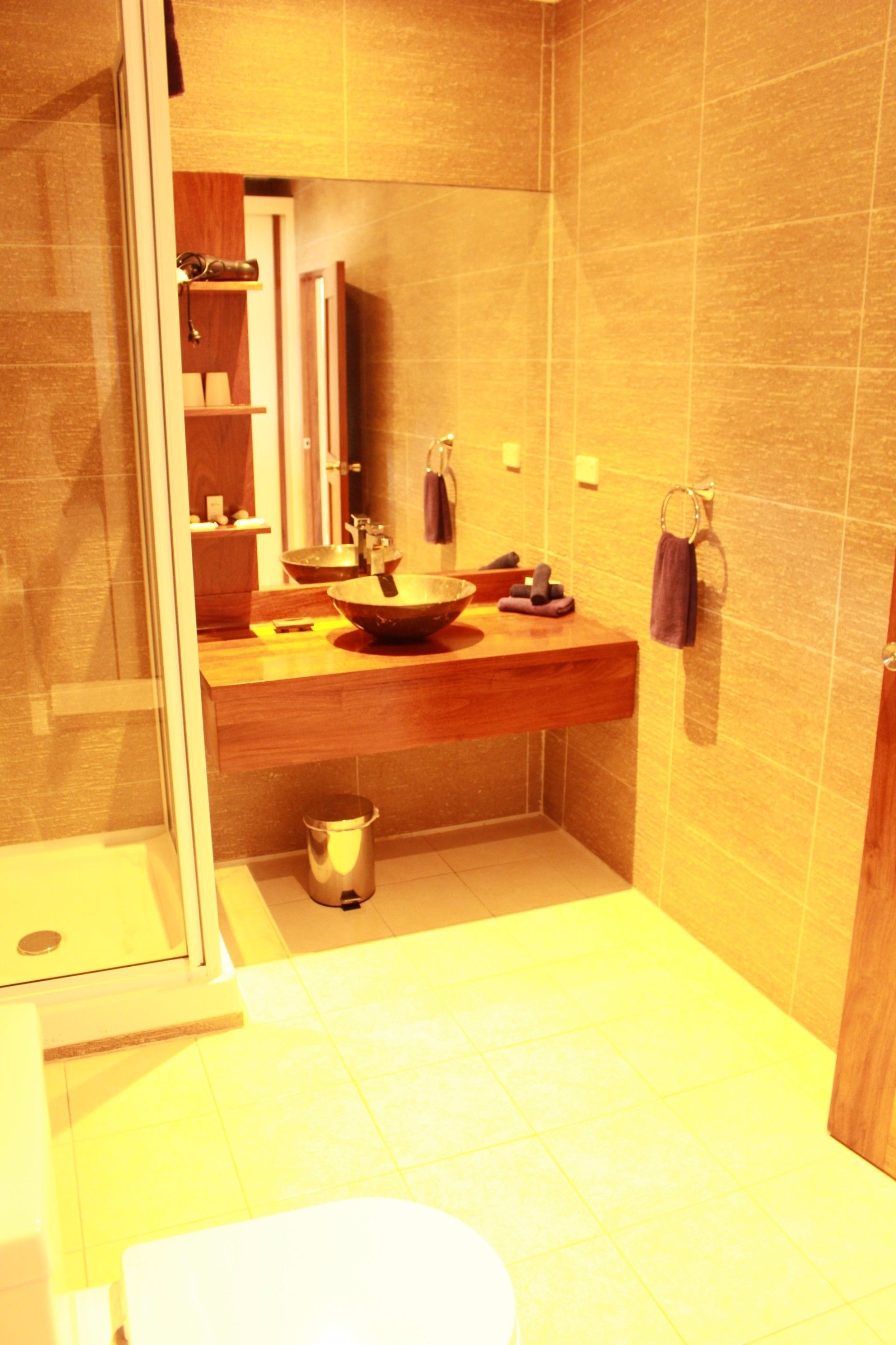 A modern bathroom with a large mirror, a wooden vanity, a vessel sink, and a glass-enclosed shower.