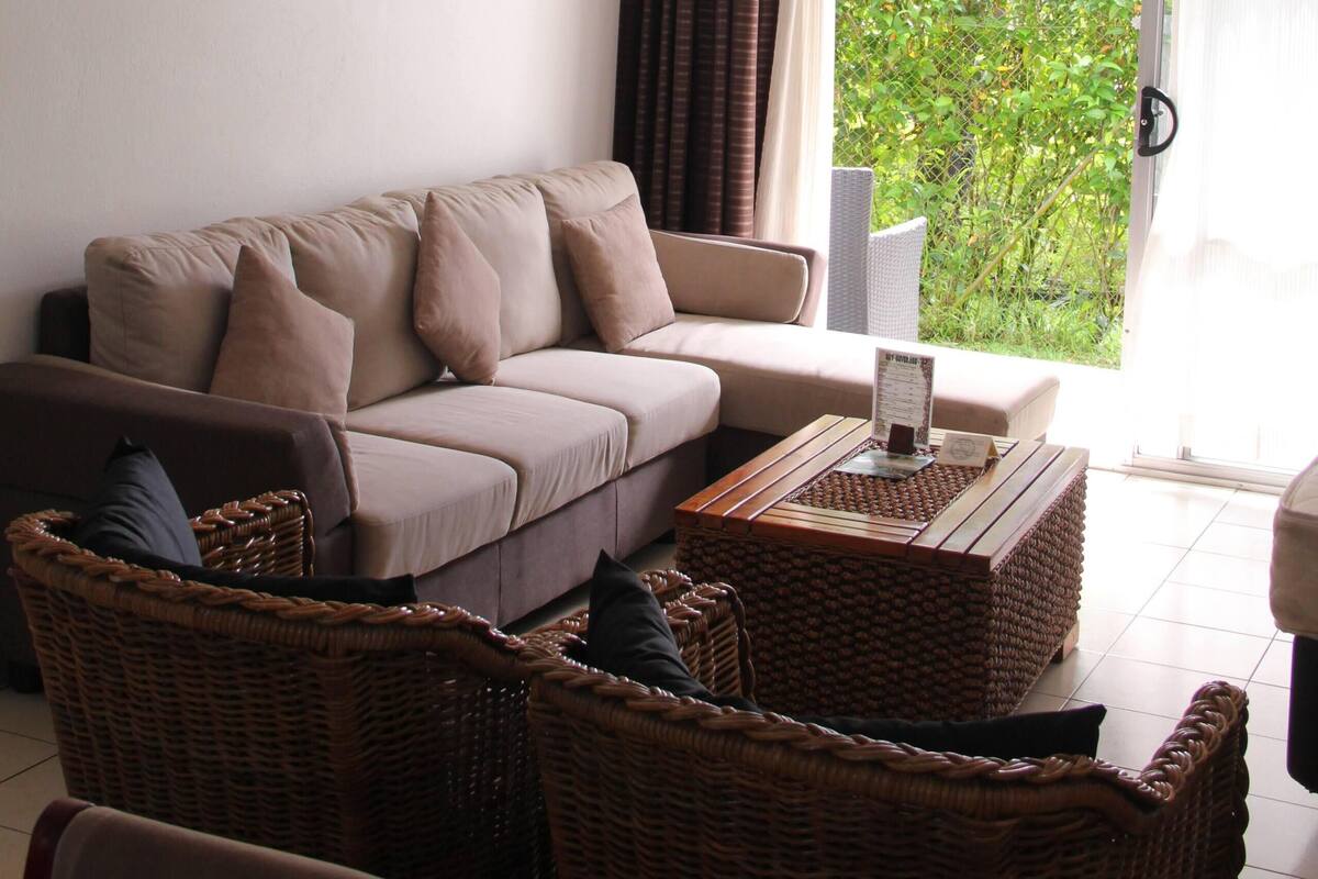 A living room with a sofa, wicker chairs, a coffee table, and a ceiling fan.