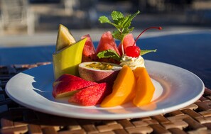 A plate of fruit including watermelon, mango, apple, and passion fruit, garnished with mint and a cherry, on a table with a blurred background.