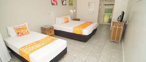 Une chambre d’hôtel avec deux lits, une petite table de chevet, une commode, un miroir et une armoire.