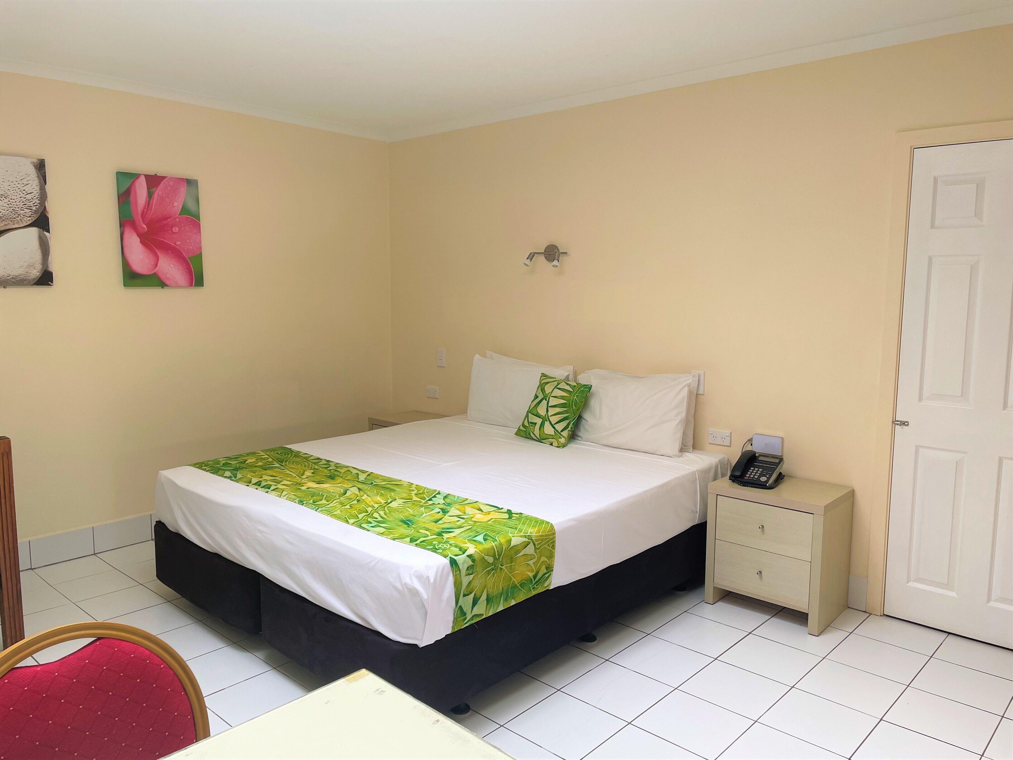 A hotel room with a bed, a bedside table with a phone, a chair, and a door.