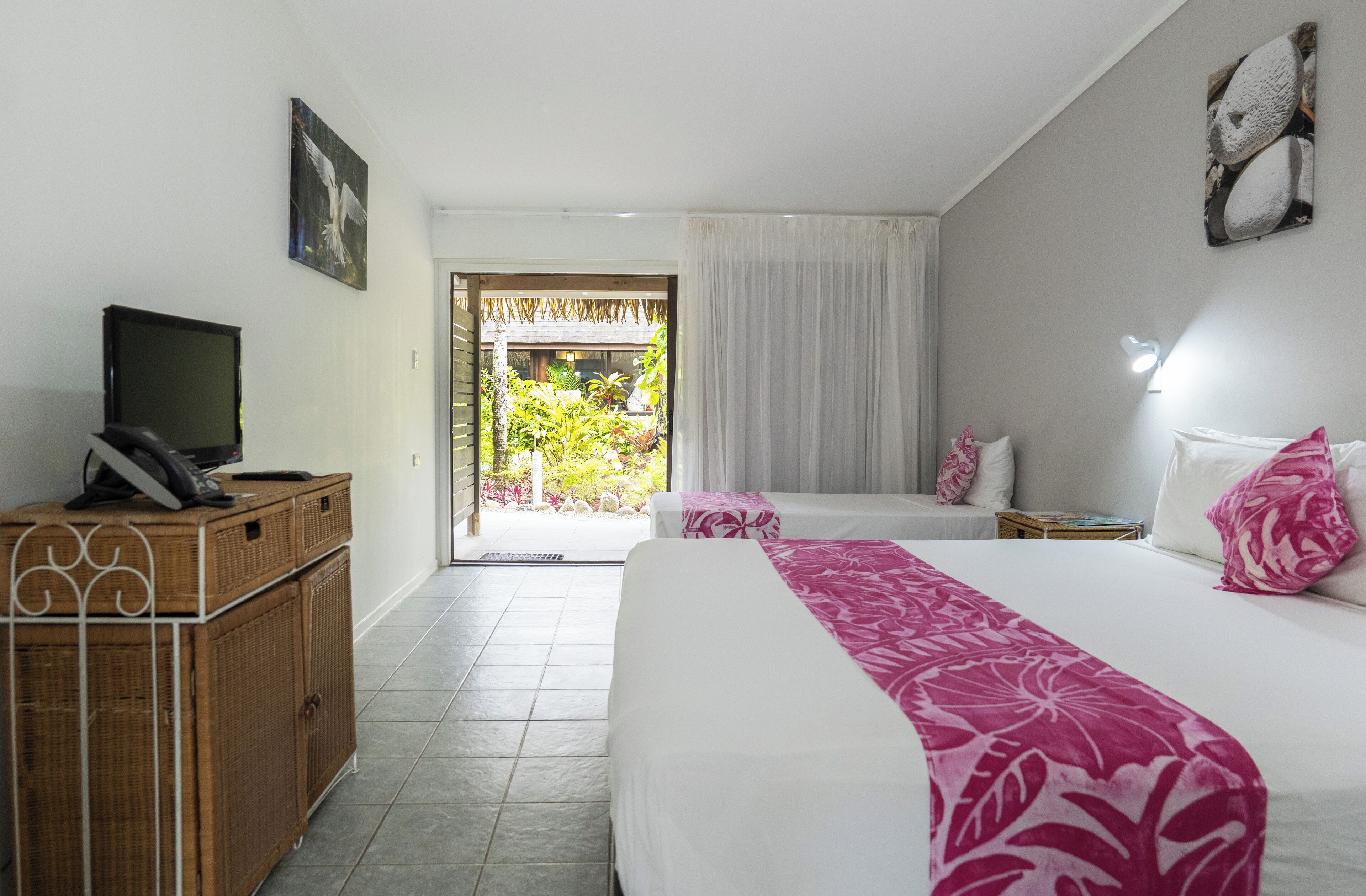 Habitación de hotel con una cama, un televisor sobre un mueble de madera y vista a un jardín a través de una puerta.