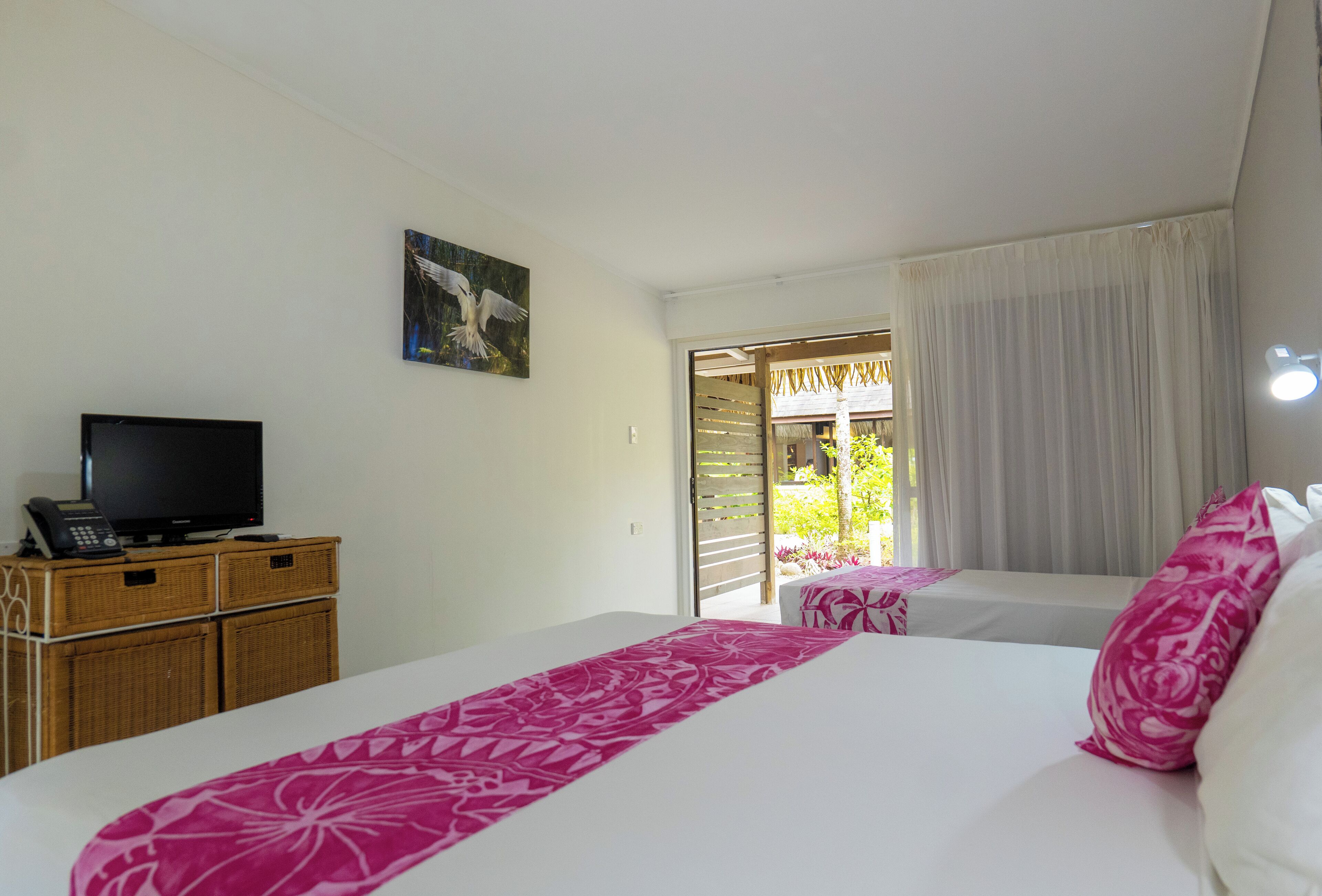 A hotel room with a bed, a television on a wooden cabinet, and a painting on the wall.