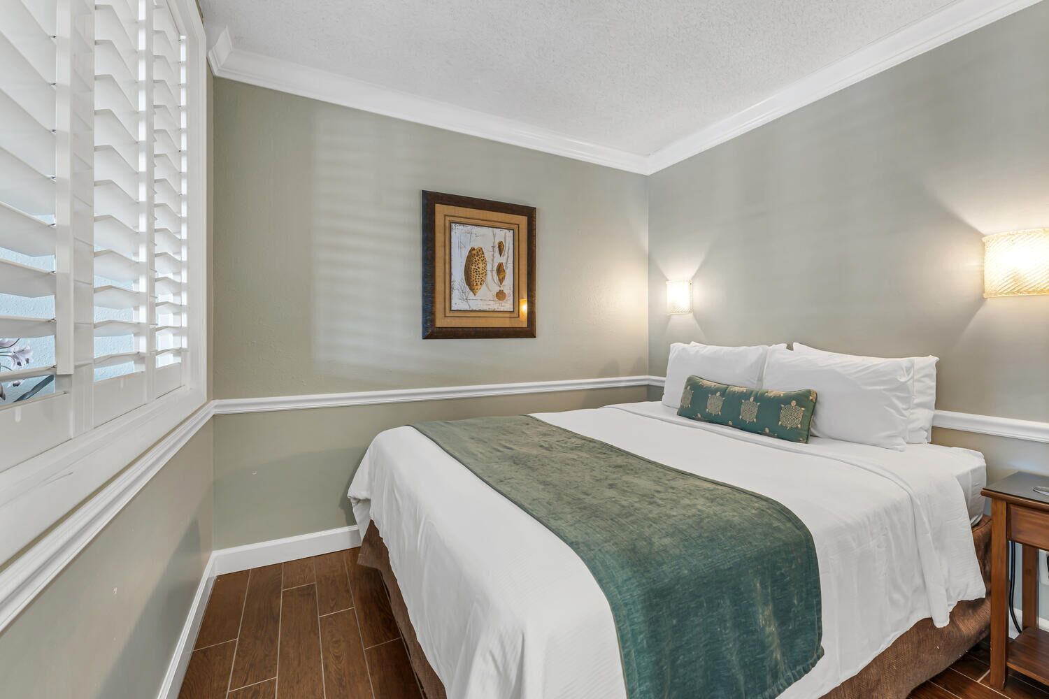 A hotel room with a large bed, a framed picture on the wall, and a window with blinds.