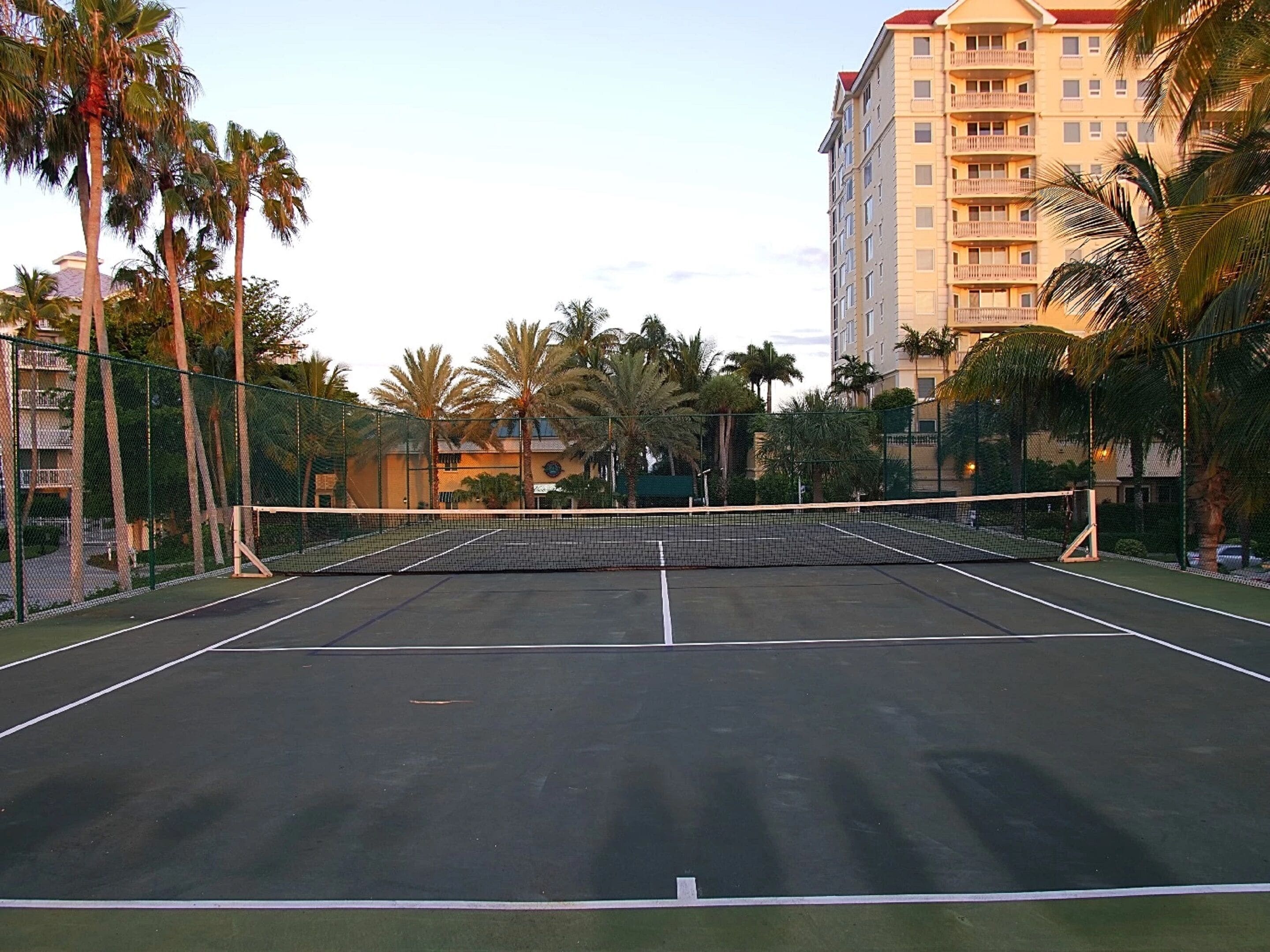 Un court de tennis en plein air, entouré de palmiers et bordé par un bâtiment d’hôtel.