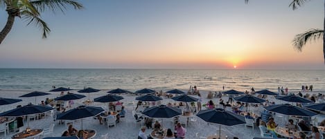 A beachside restaurant with outdoor seating and umbrellas, overlooking the ocean.
