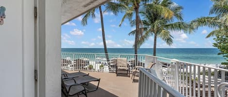 A balcony with a view of the ocean, palm trees, and a white railing.