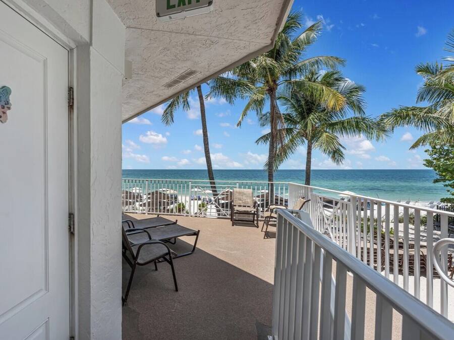 A balcony with a view of the ocean, palm trees, and a white railing.