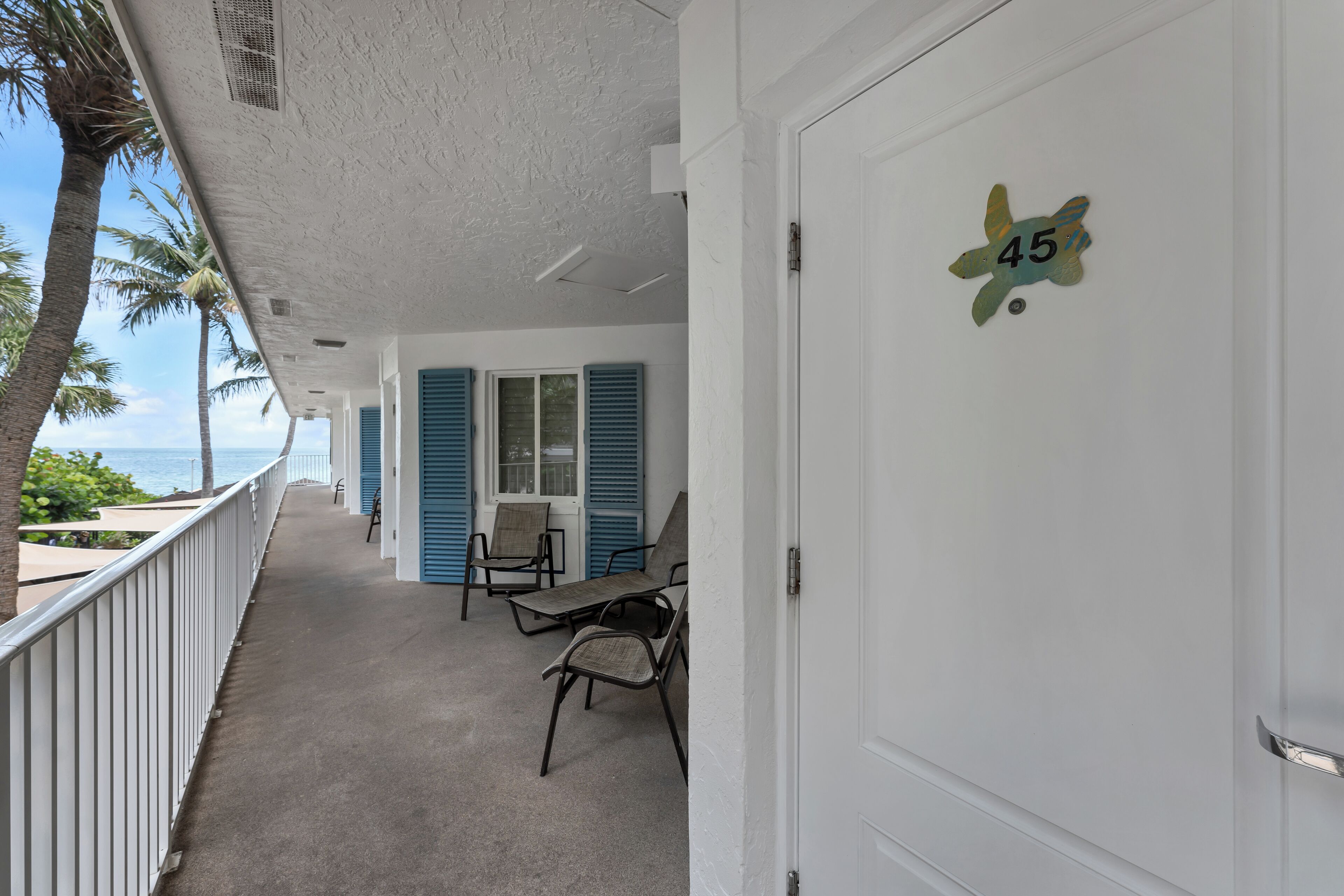 A balcony with a view of the ocean, a door with the number 45, and blue shutters on the windows.